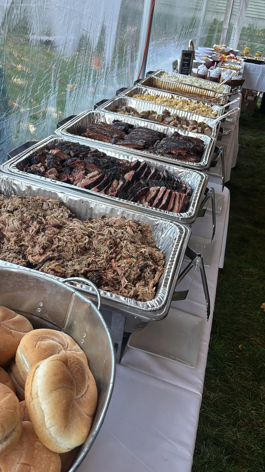 A long buffet in a white tent with pulled pork, brisket, and ribs up front